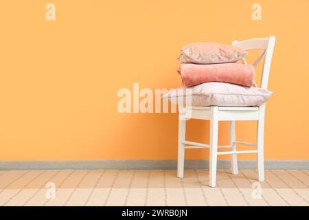 Chair with stack of pillows and folded warm plaid near orange wall Stock Photo