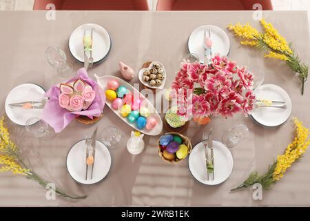 Festive stylish table setting with mimosa flowers, Easter cake and painted eggs Stock Photo