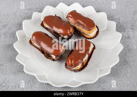 Eclairs with chocolate topping on serving plate. Traditional french eclairs with chocolate. Mini vanilla eclairs with chocolate frosting. Stock Photo