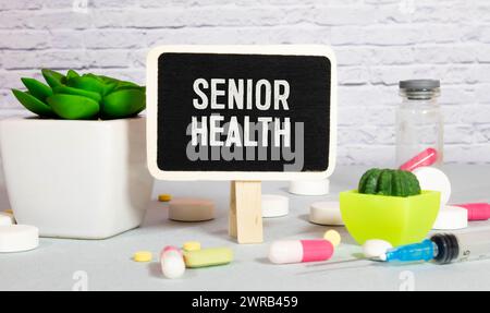 A notebook with the text SENIOR HEALTH is neatly folded among the pills, a stethoscope, and a yellow notebook. Medical concept Stock Photo