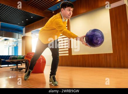 Bowler player prepares to release purple ball in modern bowling alley. Stock Photo