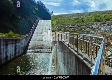 Dam with a sheet of water flowing over its edge, surrounded by mountains, in South Korea Stock Photo