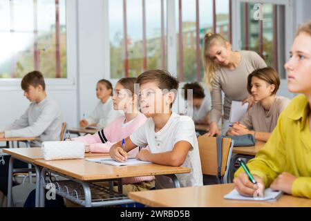 Boys and girls sitting at desk in classroom full of pupils during lesson Stock Photo
