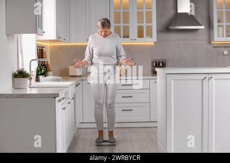 Menopause, weight gain. Concerned woman standing on floor scales in kitchen Stock Photo