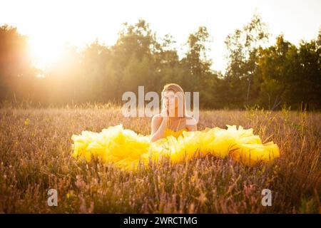A contemplative woman sits amidst a field of wildflowers, bathed in the soft, golden light of the setting sun, her vibrant yellow dress merging with the golden hues of nature. Golden Hour Dreams: Woman in a Vibrant Yellow Dress Amidst Wildflowers. High quality photo Stock Photo