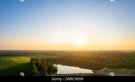 This photograph presents the first light of dawn breaking over a serene countryside landscape. A small lake sits quietly amidst fields and trees, reflecting the early morning sky. The soft light of the sun brings a gentle warmth to the cool tones of the early day, while a subtle mist in the distance creates a layer of mystique. This image encapsulates the essence of a new day's peaceful beginning in a rural setting. Dawn's Early Light Over Countryside Lake. High quality photo Stock Photo