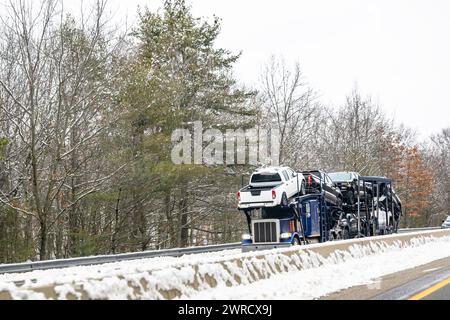 Industrial carrier car hauler blue big rig semi truck tractor transporting pick up trucks on the modular semi trailer driving on the winter highway ro Stock Photo