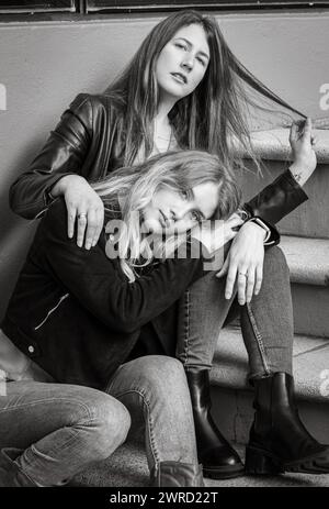 Two female friends sitting on urban stairs in grayscale Stock Photo
