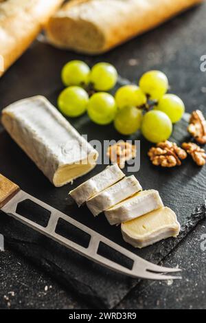 Detailed close-up of a cut Brie cheese accompanied by crisp grapes on a black slate surface, highlighting texture and form Stock Photo