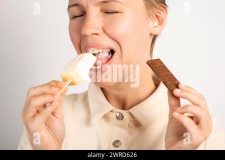 A woman indulging in ice cream and chocolate on a stick, portraying her love for sweets against a white backdrop Stock Photo