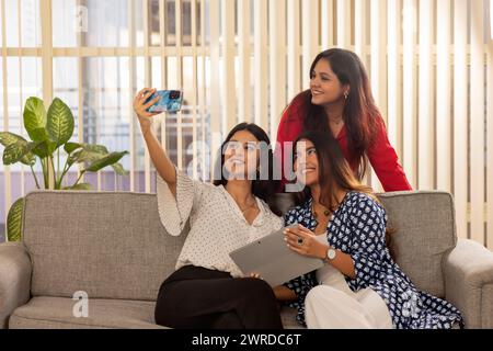 Colleagues taking selfie while working together on a digital tablet on sofa in office. Stock Photo