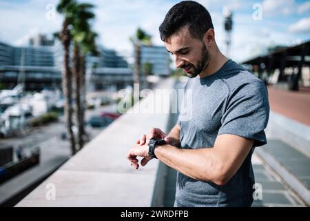Active man looking swatch during exercise outside. Fitness male looking his smartwatch checking running time after cardio training.  Stock Photo