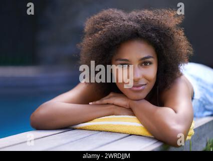 Deck, portrait and black woman relax at poolside for travel, break or chilling in a backyard on vacation. Face, smile and African female person at a Stock Photo