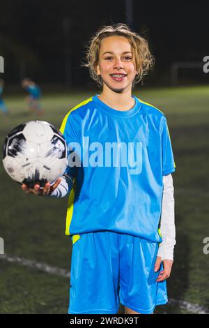 cheerful and happy little girl in a blue uniform holding a soccer ball and taking a photo. High quality photo Stock Photo