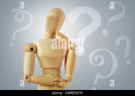 Wooden mannequin in thinking pose with quesion marks - Concept of question thinking and doubts Stock Photo
