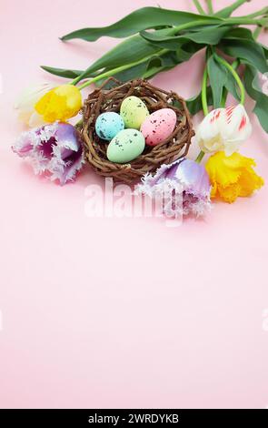 Multi-colored spotted eggs in nest with tulips on pink background. Easter. Vertical. Copy space Stock Photo