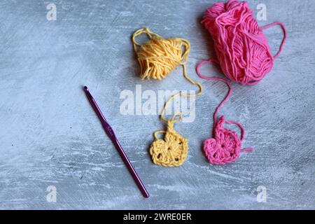 Soft cotton yarn, crochet hook and crochet project in process on grey stone background. Top view with copy space. Hobbies and leisure concept. Stock Photo