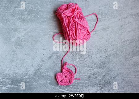 Soft cotton yarn, crochet hook and crochet project in process on grey stone background. Top view with copy space. Hobbies and leisure concept. Stock Photo
