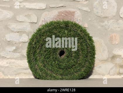 roll of green synthetic grass near stone wall Stock Photo