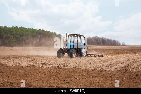 A spring day the tractor goes and pulls a plow plowing a field before landing of crops. Stock Photo