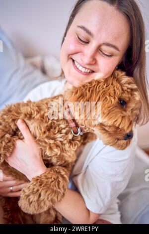 a  young woman playing and kissing cockapoo girl on bed, minimalism Stock Photo