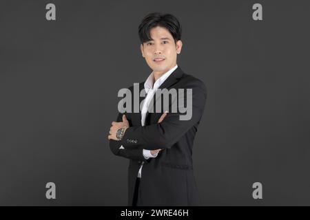 Businessman wearing a black suit stands with his arms crossed on a black background. Stock Photo