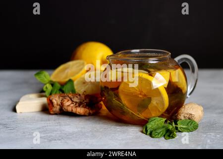 Still life with glass teapot, lemons and mint leaves on a table. Healthy homemade drink closes up photo. Stock Photo