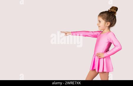 Portrait of a little gymnast girl in pink dress pointing with index finger to one side picture for advertising banners or promotions. High quality pho Stock Photo