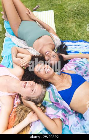 Three women are lying on a blanket, laughing together in an outdoor setting Stock Photo