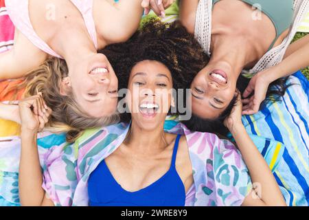 Three women are lying on a colorful blanket, heads together, smiling joyfully Stock Photo