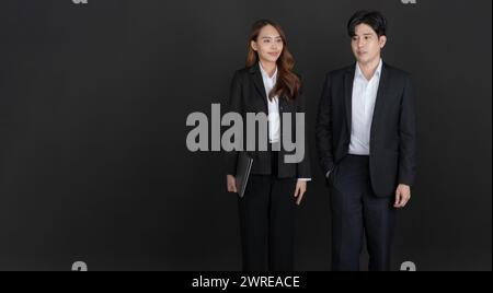 Businessman and businesswoman discussing business and smiling while walking together in studio on black background. Stock Photo