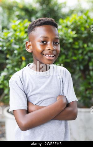 African American boy stands with arms crossed, smiling in an outdoor setting in a garden Stock Photo