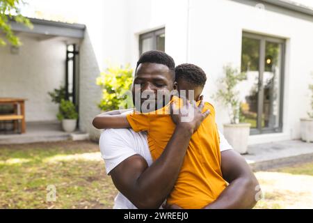 African American father embraces his son in a warm hug outdoors in the backyard Stock Photo