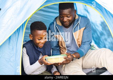 African American father and son share a moment inside a tent, holding a container Stock Photo