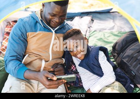 African American father and son share a moment inside a tent, looking at a smartphone Stock Photo