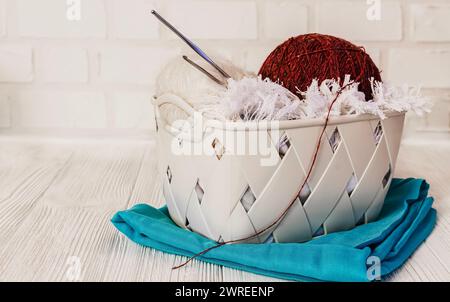 Multi-colored threads, skeins and balls of wool yarn, knitting needles, in a box, on a white brick background. Concept of knitting, needlework, handma Stock Photo