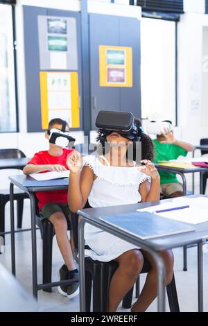 Biracial children are engaged with virtual reality headsets in a classroom at school Stock Photo