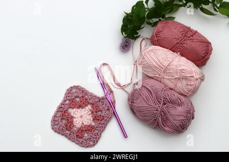 Pink crocheted granny square, soft  cotton yarn balls of different pink color shades. White background with copy space. Spring crochet concept. Stock Photo