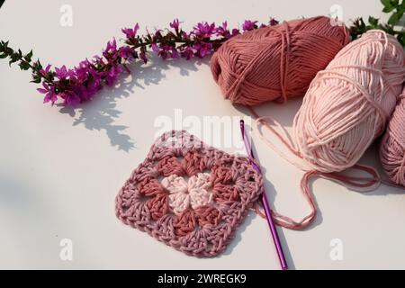 Pink crocheted granny square, soft  cotton yarn balls of different pink color shades. White background with copy space. Spring crochet concept. Stock Photo