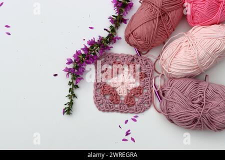 Pink crocheted granny square, soft  cotton yarn balls of different pink color shades. White background with copy space. Spring crochet concept. Stock Photo