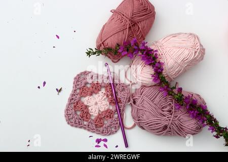 Crochet pattern, flowers, cotton yarn balls top view photo. Granny square made of soft pink organic yarn. Handmade crochet pattern on white background Stock Photo