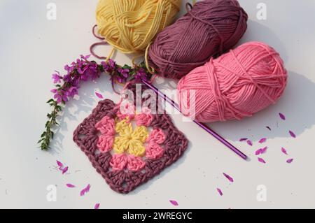 Pink crocheted granny square, soft  cotton yarn balls of different pink color shades. White background with copy space. Spring crochet concept. Stock Photo