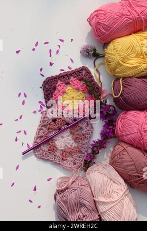 Pink crocheted granny square, soft  cotton yarn balls of different pink color shades. White background with copy space. Spring crochet concept. Stock Photo