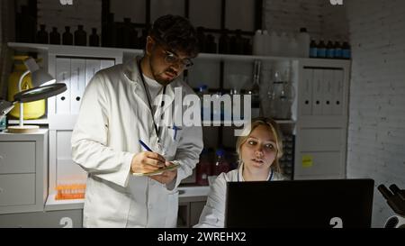 A man and woman, scientists, collaborate using a laptop and taking notes in a laboratory setting. Stock Photo