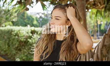 Cool, young hispanic woman capturing nature's sunlight with a relaxed yet serious expression. beautifully combing hair by hand while standing in green Stock Photo
