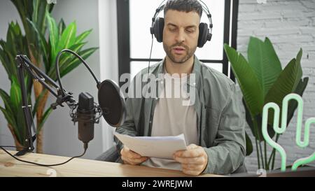 Handsome bearded man in headphones reading script indoors at a modern radio studio. Stock Photo