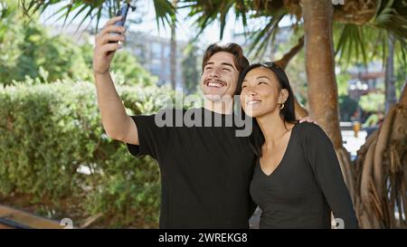 A smiling interracial couple takes a selfie on a sunny park day. Stock Photo