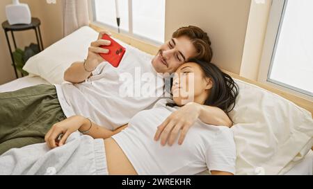 A loving interracial couple, a man and a woman relaxing together in a cozy bedroom, capturing a selfie Stock Photo