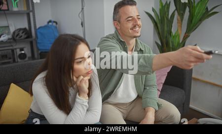 An engaged man and bored woman sitting on a couch in a modern living room, home entertainment. Stock Photo