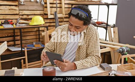 Handsome man with curly hair using a tablet in a well-equipped carpentry workshop Stock Photo